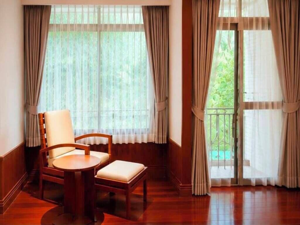 A room with a wooden floor, a round table, a cushioned chair, and a view through a window with curtains.