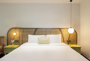 Una cama bien hecha con un cabecero estampado, mesitas de noche con lámparas y una silla sencilla.