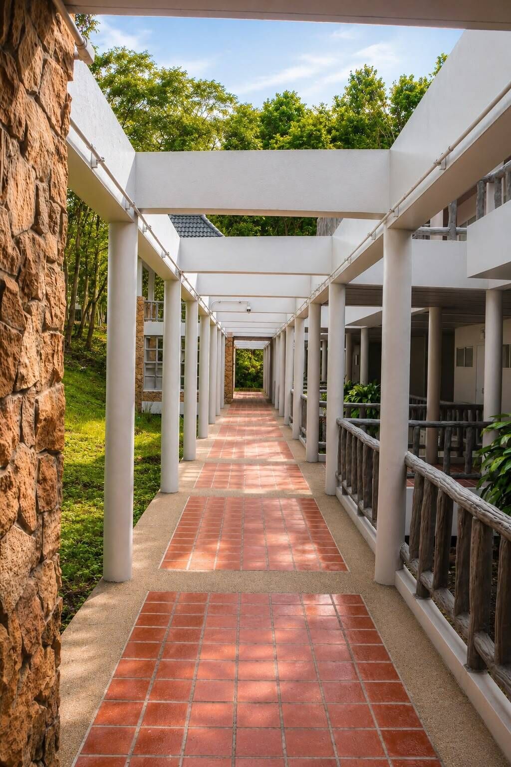 A covered walkway with columns, a stone wall on one side, and a view of greenery in the background.