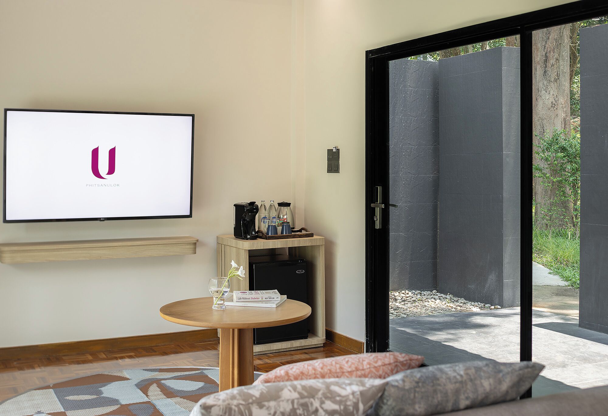 A modern room with a flat-screen TV, a small table with a coffee machine, a sofa, and a sliding glass door leading to an outdoor area.