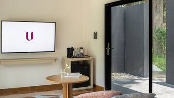 A modern room with a flat-screen TV, a small table with a coffee machine, a sofa, and a sliding glass door leading to an outdoor area.