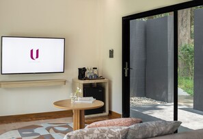 Una habitación moderna con televisión de pantalla plana, una pequeña mesa con cafetera, un sofá y una puerta corrediza de vidrio que da a un área exterior.