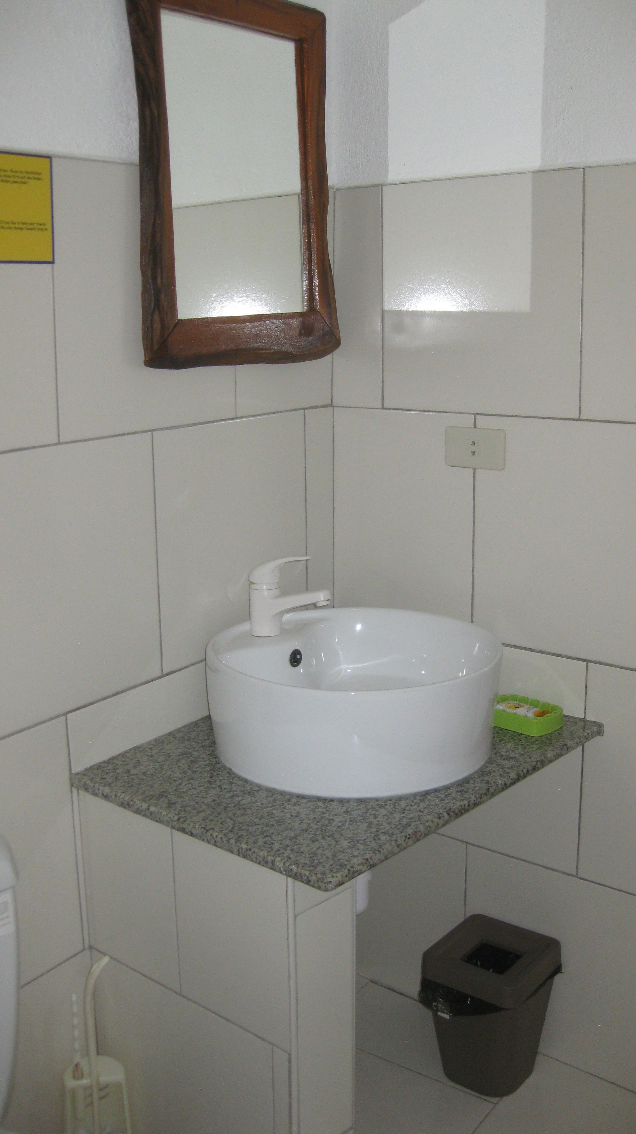 Un baño con un lavamanos blanco, un espejo y un cubo de basura.