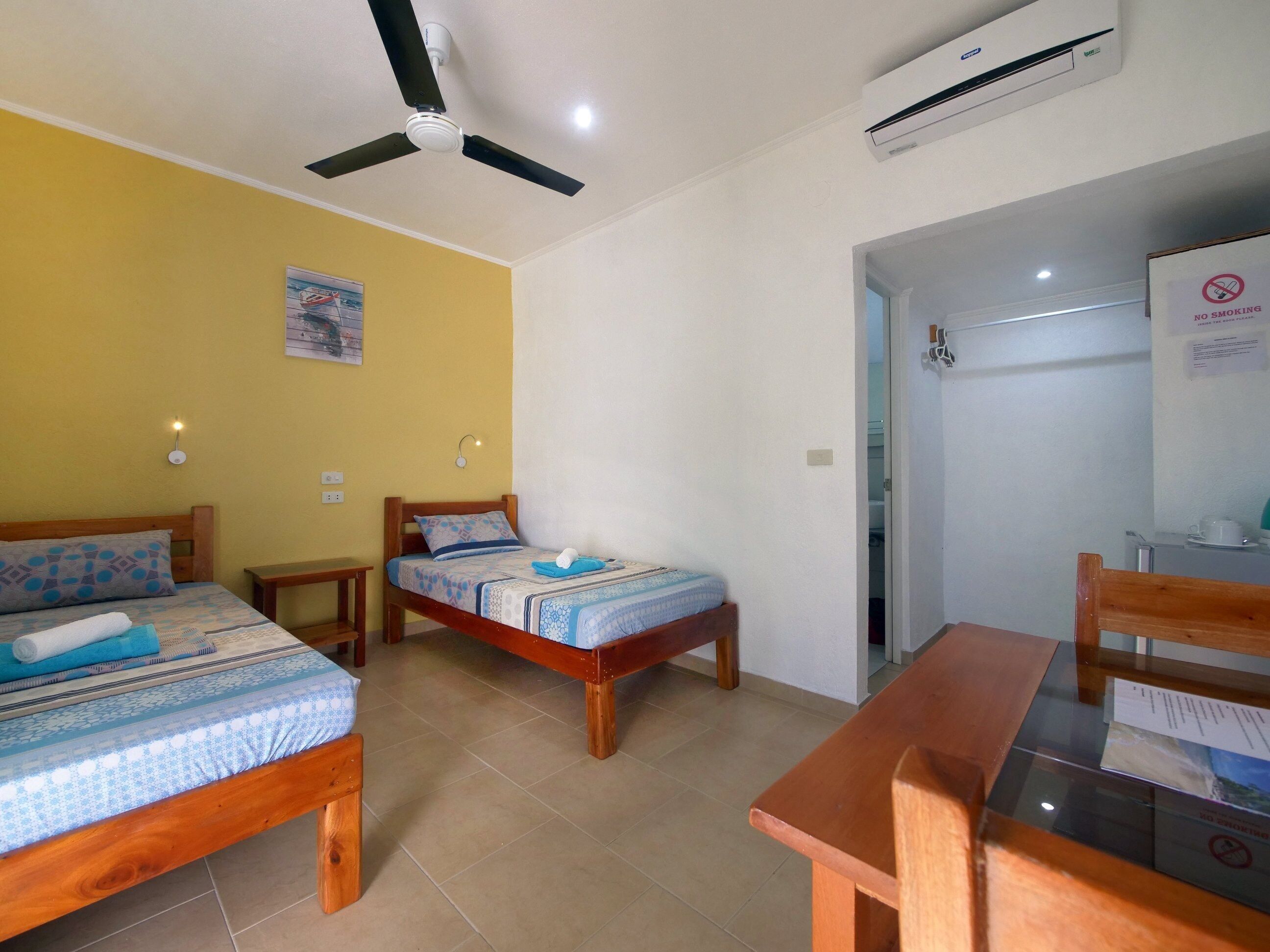 A room with two wooden beds, a ceiling fan, an air conditioner, and a table with chairs.