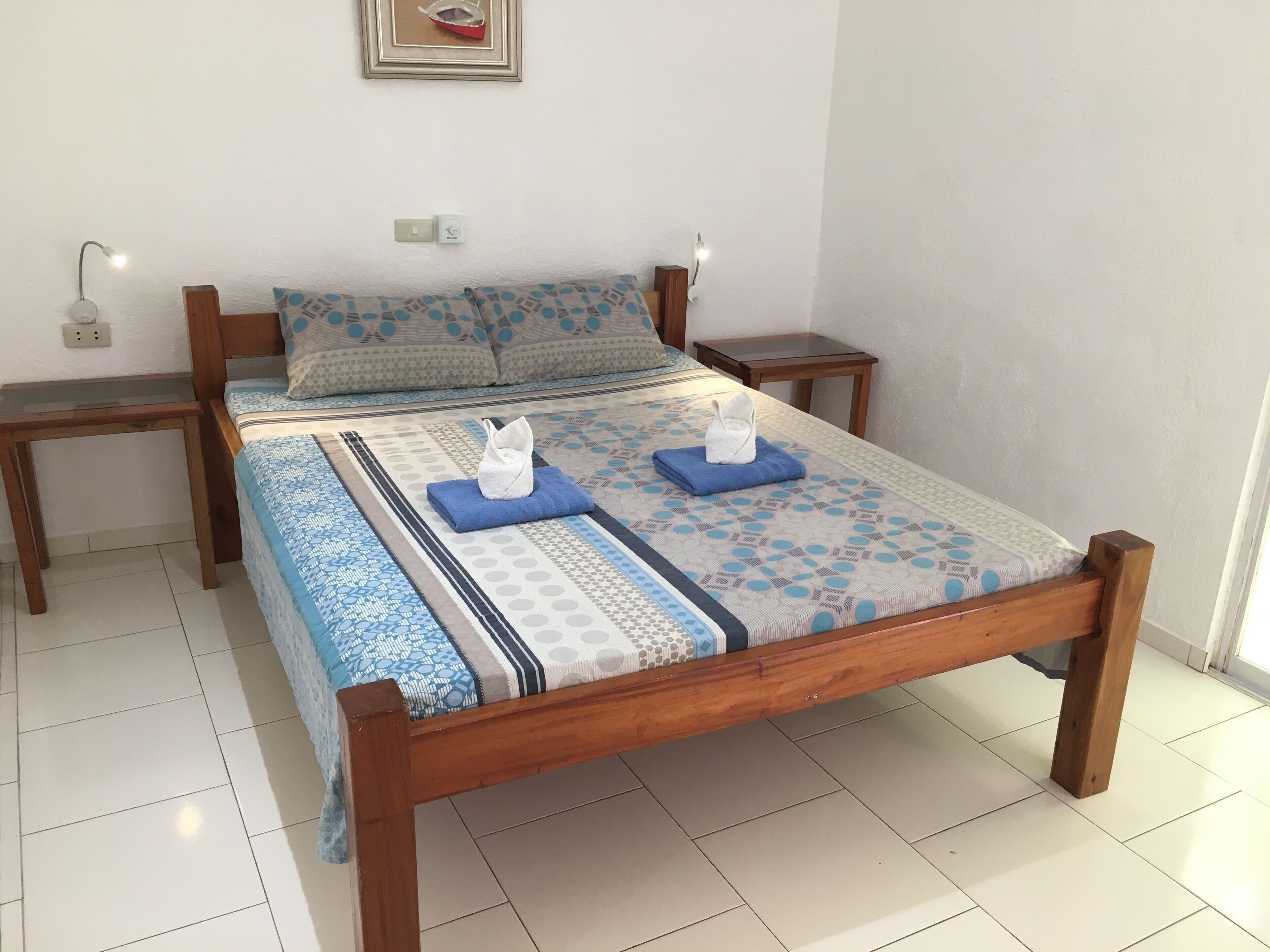 A neatly made bed with a patterned bedspread, two pillows, and two folded towels on the bed.