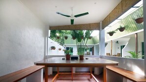 A room with a wooden table, benches, a ceiling fan, and potted plants. - Alona Gecko Inn (Panglao)