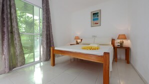 A bedroom with a wooden bed, two bedside tables with lamps, a window with curtains, and a framed picture on the wall. - Alona Gecko Inn (Panglao)