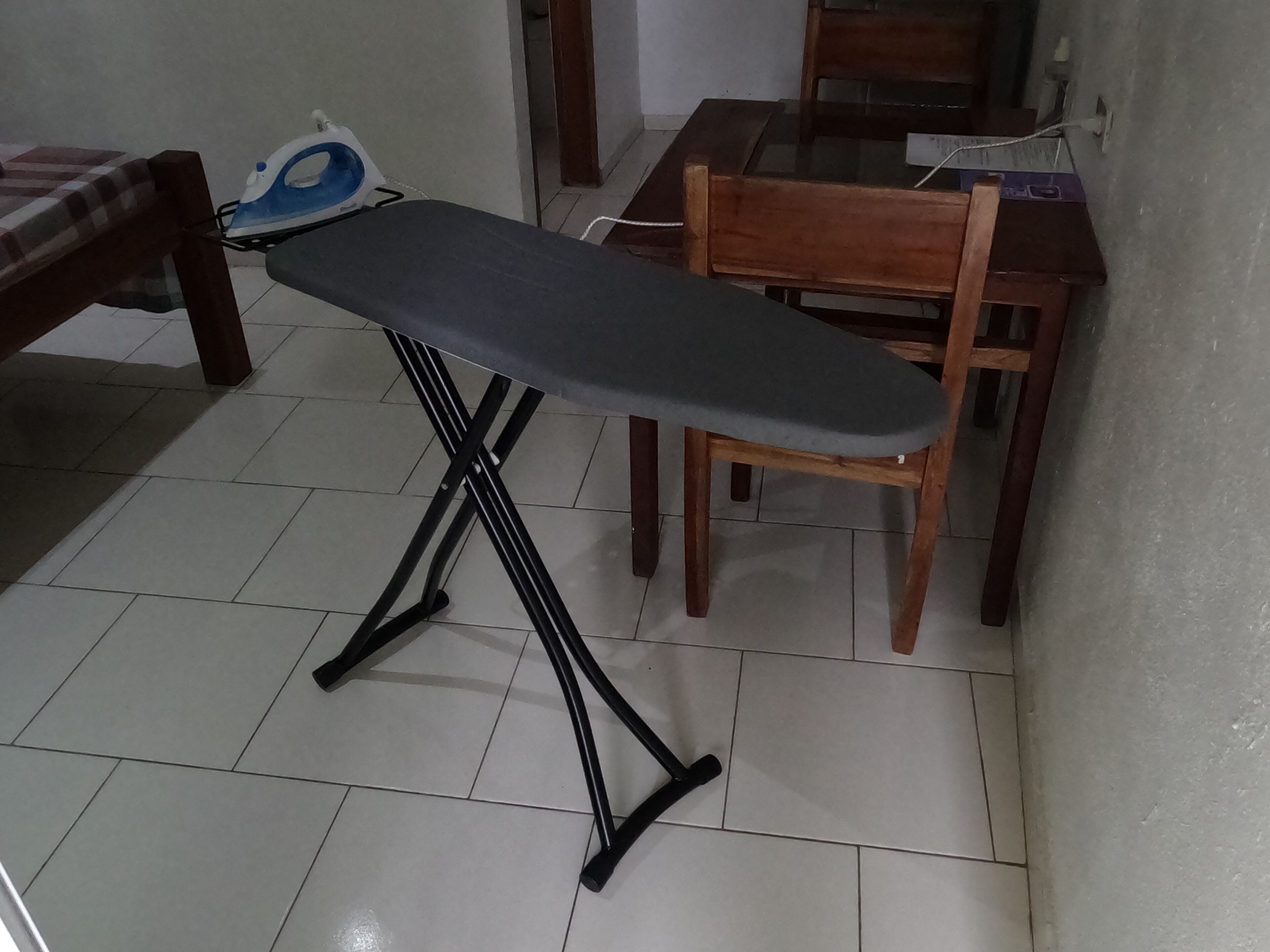 A room with a wooden dining table, a chair, and a black ironing board with an iron.