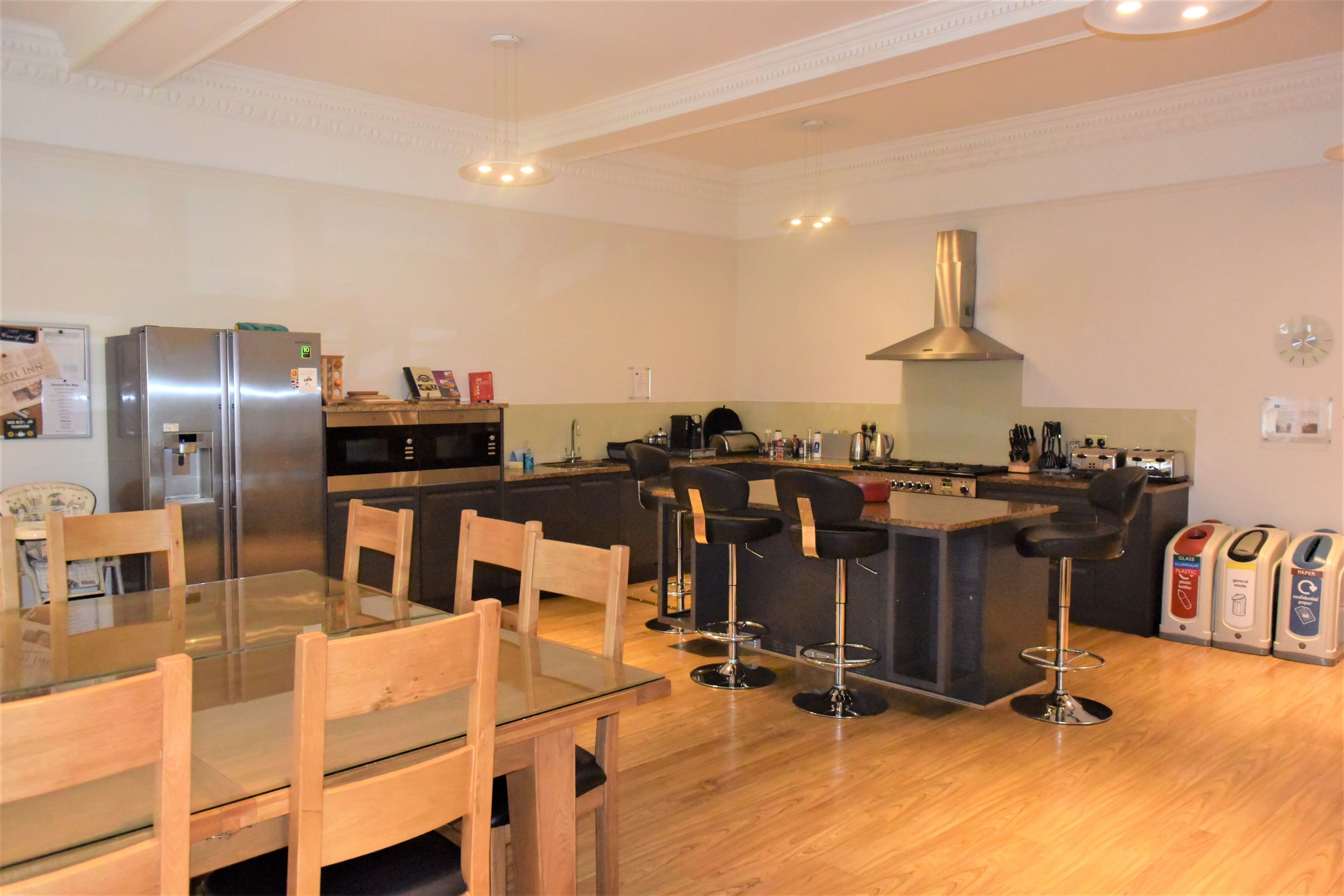 A modern kitchen with a central island, bar stools, a stainless steel refrigerator, and a built-in oven.