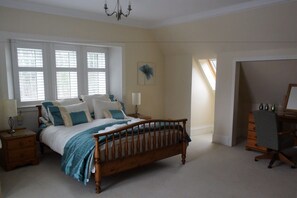Een slaapkamer met een houten bed, een nachtkastje, een dressoir en een bureau.