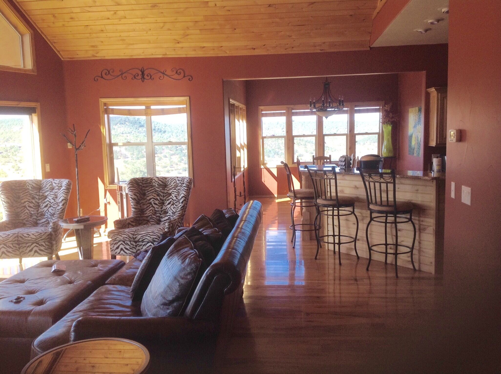 A spacious living room with a wooden ceiling, a large sofa, a zebra-patterned armchair, and a dining area with bar stools.
