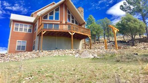 A two-story house with a balcony, surrounded by a stone wall and a grassy area.