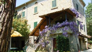 A stone building with a covered porch and purple flowers.