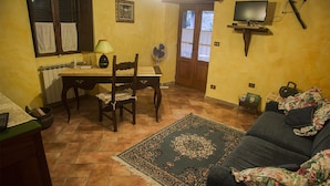 A cozy living room with a sofa, a dining table with chairs, a television mounted on the wall, and a patterned rug on the floor.
