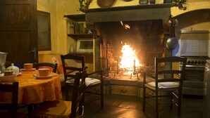 A cozy dining area with a fireplace, wooden chairs, a table set with dishes, and a kitchen area with a stove.