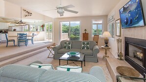 A spacious living area with a sofa, coffee table, and a fireplace. There is a television mounted on the wall and a ceiling fan. - Waterfalls, Palm Trees, and Hanalei Bay,  Short walk to beaches and resorts (Princeville)