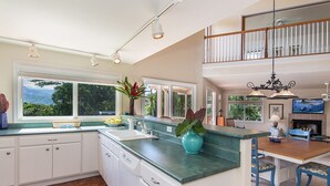 A spacious kitchen with a large island, white cabinetry, and a view of greenery outside. - Waterfalls, Palm Trees, and Hanalei Bay,  Short walk to beaches and resorts (Princeville)