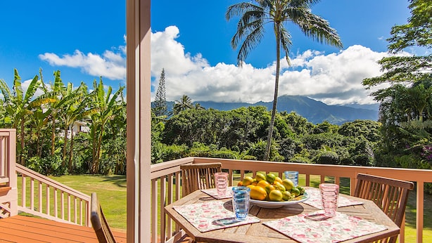 A wooden deck with a table set for dining, overlooking a lush garden and mountains. - Waterfalls, Palm Trees, and Hanalei Bay,  Short walk to beaches and resorts (Princeville)