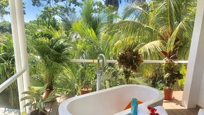 Ein Badezimmer mit Badewanne, Topfpflanzen und Blick auf üppiges Grün.