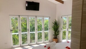 Ein Schlafzimmer mit einem großen Bett, einer Topfpflanze und einem an der Wand befestigten Fernseher.