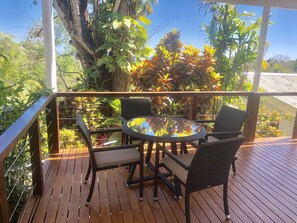 A wooden deck with a glass table and chairs, surrounded by lush tropical plants. - Chez Mu Luxury Villa - Amazing Ocean & Jungle Views 1 Mi/TownNew Pictures!!! (Montezuma)