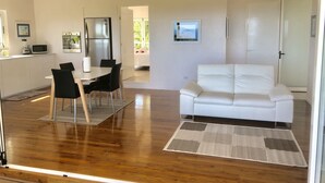 Ein modernes Wohnzimmer mit einem weißen Sofa, einem Essbereich mit Tisch und Stühlen sowie einer Küche mit Kühlschrank und Mikrowelle.