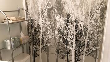A bathroom with a toilet, a sink, a shelf with towels, and a shower curtain with a tree design.