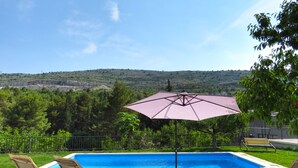 Una piscina con lettini e un ombrellone, circondata da un patio in pietra e vista su un paesaggio collinare.