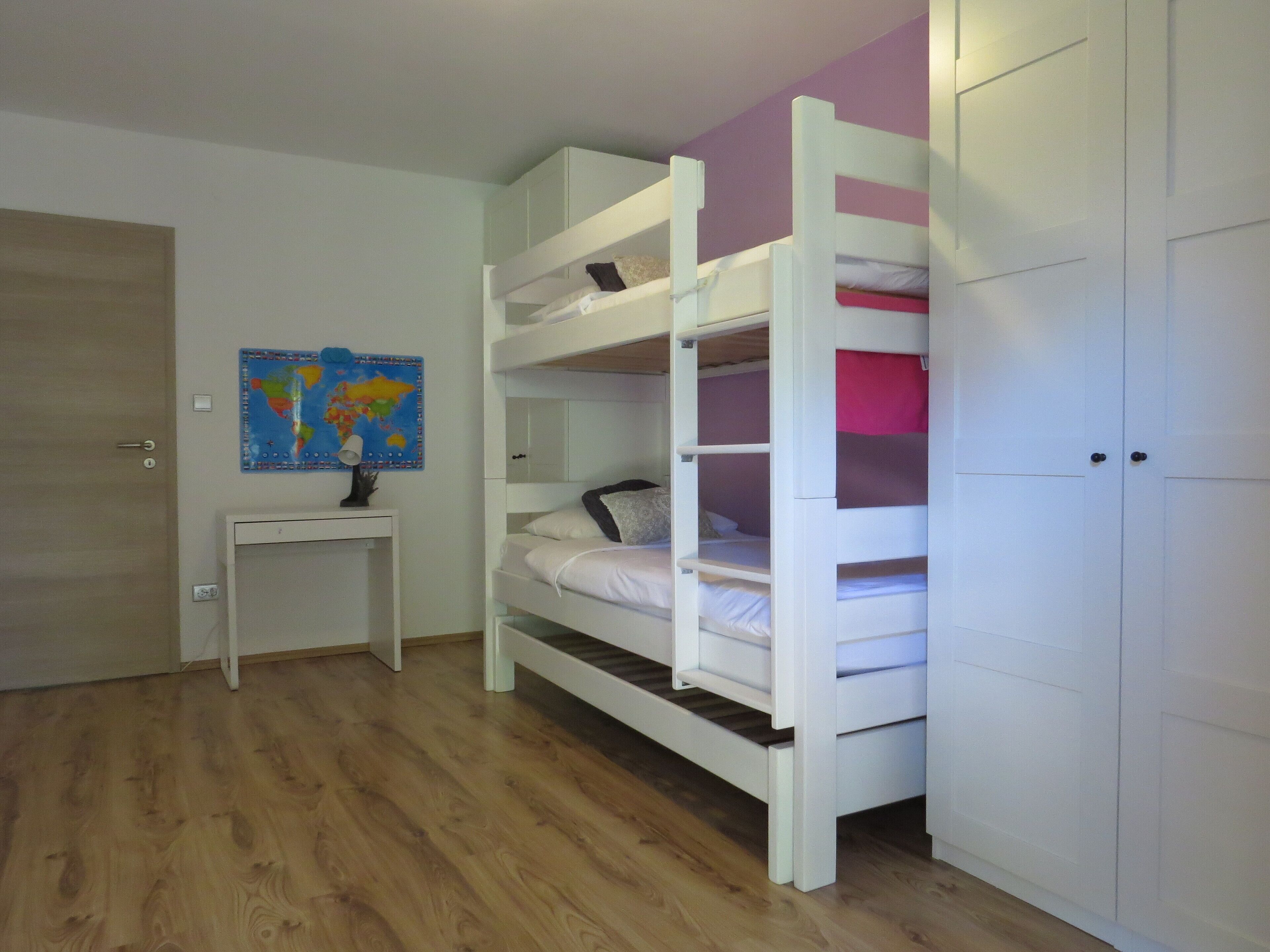 A room with a bunk bed, a desk, a map on the wall, and a wardrobe.