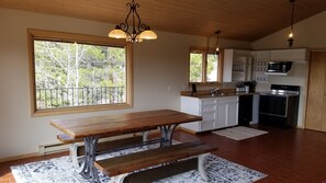 Una cocina amplia con una mesa de madera y bancos, ventanas grandes con vistas a árboles y electrodomésticos modernos.