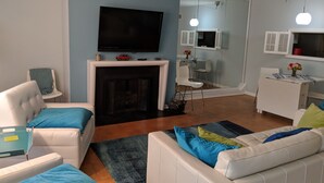 A living room with a fireplace, a television mounted above it, and a dining area with a table and chairs. - Steps to US Capitol - US Supreme Court and Monuments (Washington)