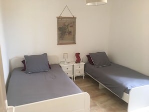 Une chambre avec deux lits simples, une table de chevet avec une lampe et un tableau accroché au mur.