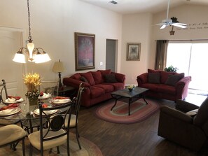 Un salon avec deux canapés rouges, une table à manger dressée pour quatre personnes et un ventilateur de plafond.
