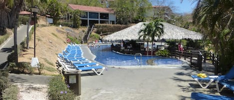 A swimming pool area with lounge chairs and a thatched-roof structure.