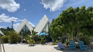 En kystnær ferieby med moderne, pyramideformede bygninger, en sandstrand og et par blå stole.