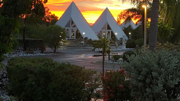 Et resort med to pyramideformede bygninger, omgivet af frodig vegetation og en solnedgangshimmel.