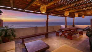 An outdoor patio with wooden furniture, a view of the ocean, and hanging lights.