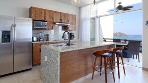 A modern kitchen with granite countertops, wooden cabinets, stainless steel appliances, and a large island with bar stools.