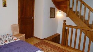 Ein Schlafzimmer mit Holztür, einem Bett mit gemustertem Überwurf, einem Sessel, einer Holztreppe und einer wandmontierten Leuchte.