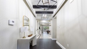 A modern hallway with a herringbone floor, a white console with a lamp, and a ceiling with exposed beams and pendant lighting.