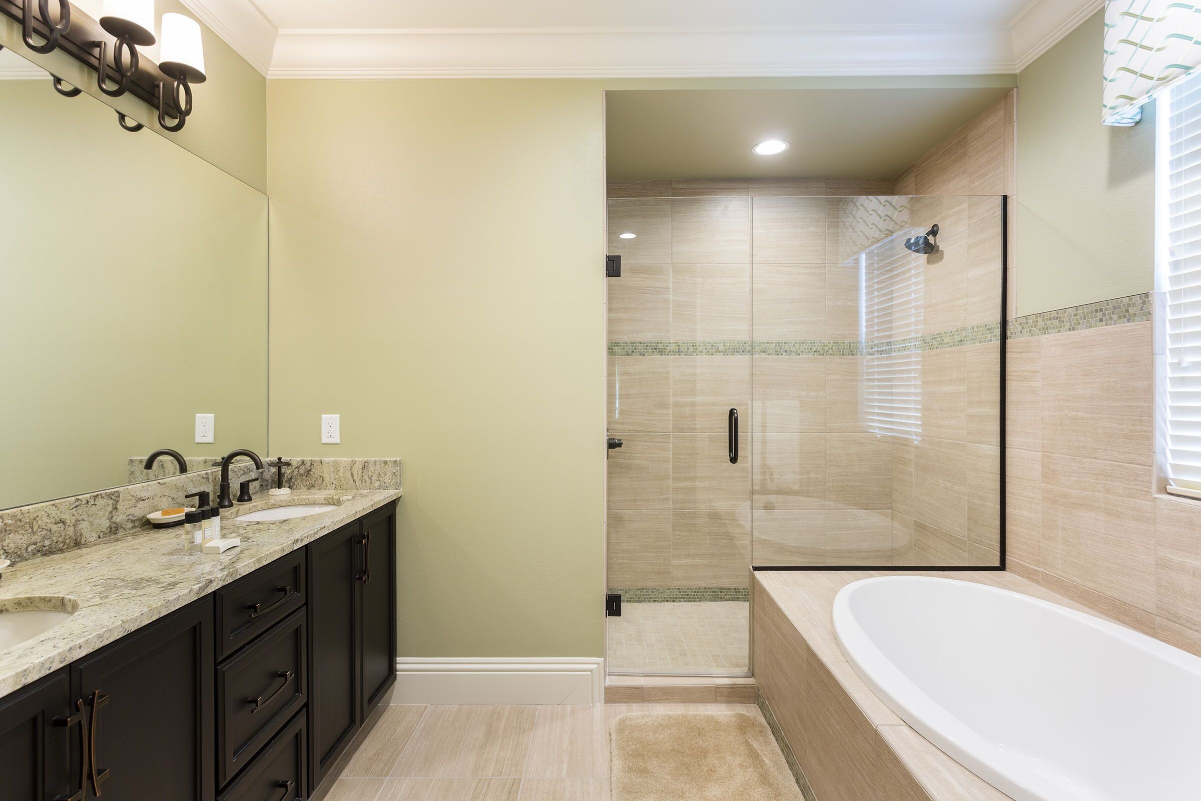 A bathroom with a large bathtub, a glass-enclosed shower, and dark cabinetry.