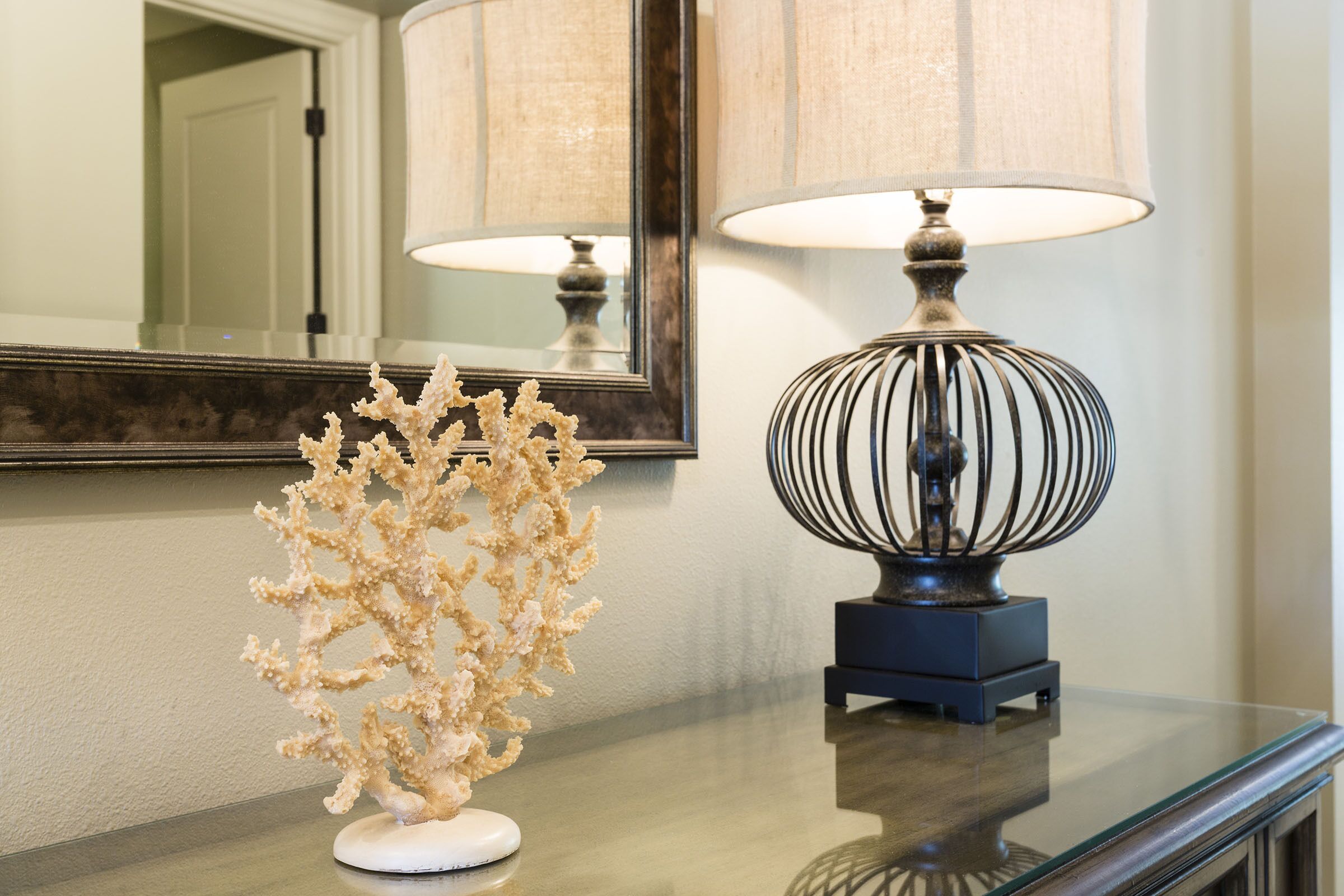 Une table en verre ornée d’un élément décoratif en forme de corail et d’une lampe avec un abat-jour à rayures.