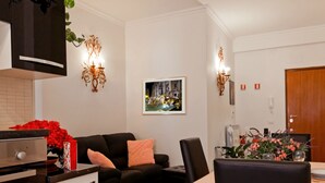 Ein modernes Wohnzimmer mit einem schwarzen Sofa, einem Esstisch mit Stühlen, einer Küchenzeile mit Herd und einem gerahmten Bild an der Wand.