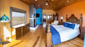 Um quarto espaçoso com uma cama grande, piso de madeira, ventilador de teto e vista pela janela.