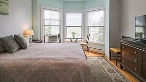 A bedroom with a bed, a dresser, a chair, and a TV. - Ocean View East End Studio in a Historic Victorian (Portland)
