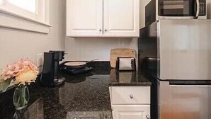 A kitchen with white cabinets, a stainless steel refrigerator, a microwave, a coffee maker, and a vase with flowers. - Ocean View East End Studio in a Historic Victorian (Portland)