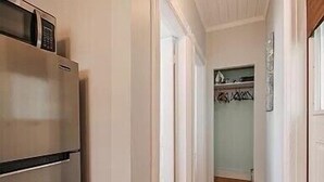 A narrow hallway with a stainless steel refrigerator on the left, a wooden floor, and a door leading to a closet with hanging clothes. - Ocean View East End Studio in a Historic Victorian (Portland)