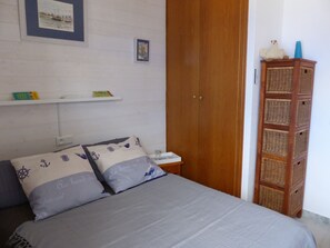 Une chambre à coucher comprenant un lit, des oreillers, une table de chevet, une armoire en bois et un meuble de rangement en osier.
