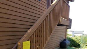 A wooden staircase leading to a house with a metal water container on the grass.