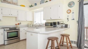 A modern kitchen with white cabinetry, a central island with stools, a microwave, and an oven.